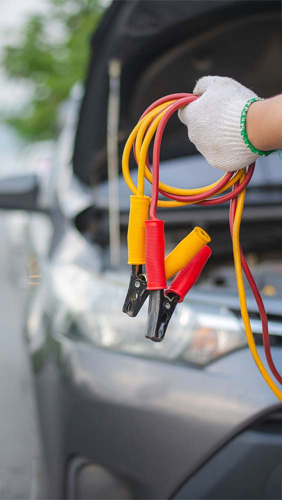Batteries & electrical jump start cables held near an open hood for battery service.