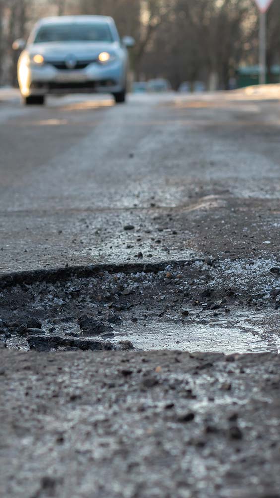 Suspension, shocks and struts service showing a pothole that can damage vehicle suspension components.