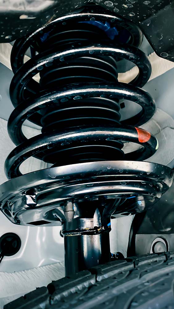 Suspension, shocks and struts service close-up of a coil spring and strut assembly inside a wheel well.